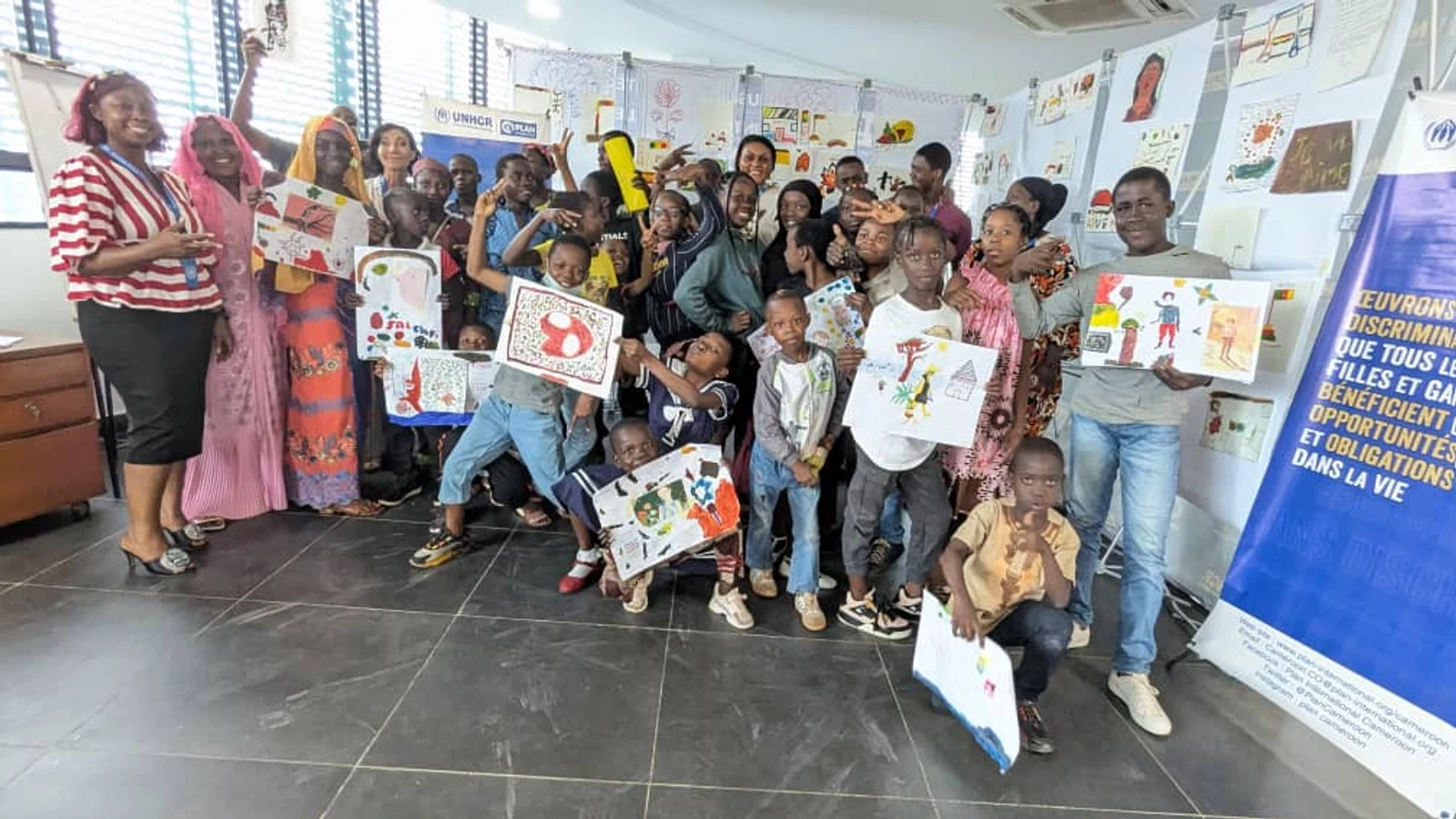 Atelier d'art-thérapie Plan International & UNHCR — enfants brandissant leurs œuvres